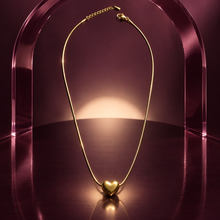 Amora gold puffed heart pendant displayed beneath a translucent plum acrylic arch