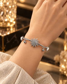 Silver starburst bangle bracelet with heart accents and dangling charms on a luxury stone surface