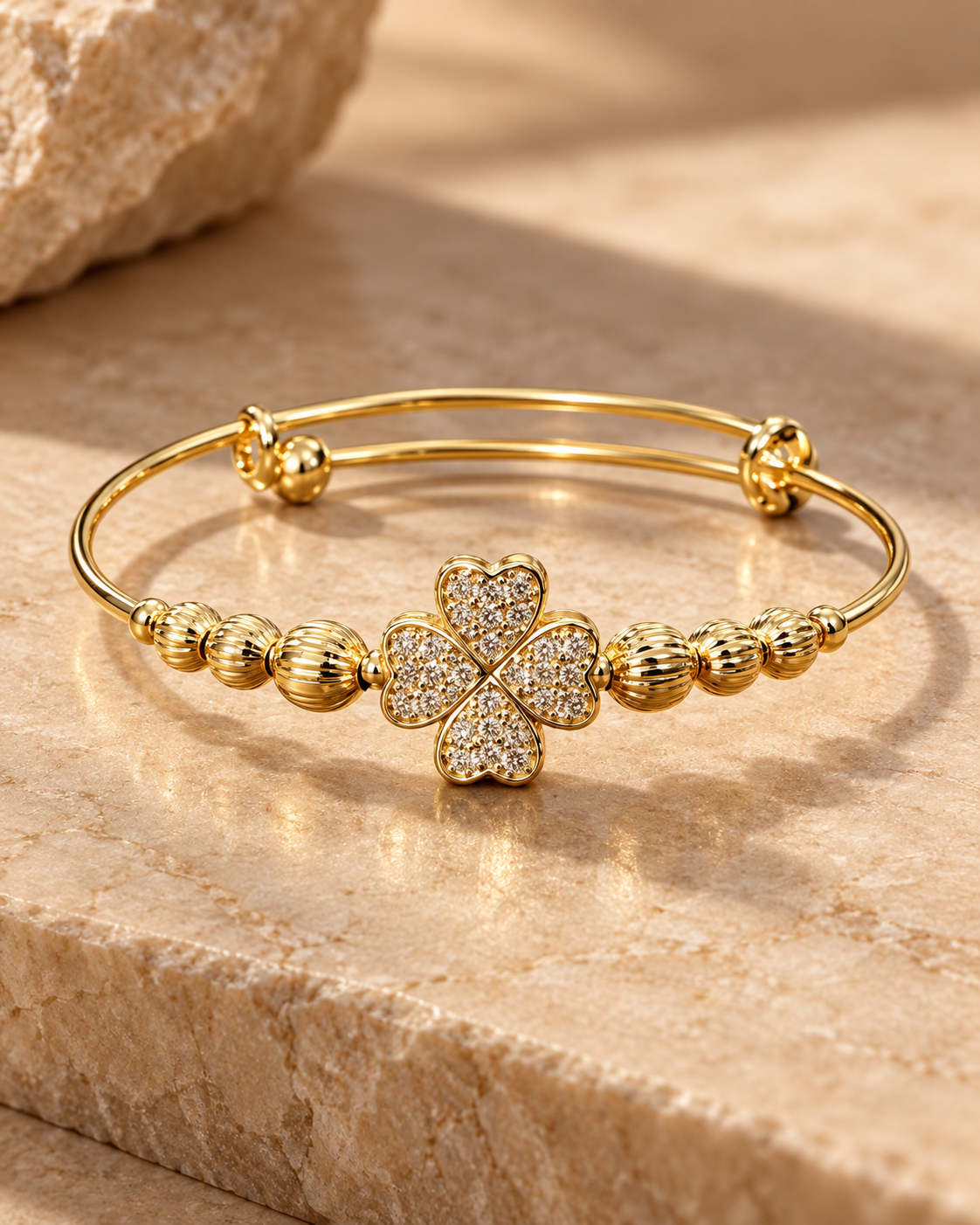 Gold clover bangle bracelet with pavé heart-shaped petals on a warm stone surface