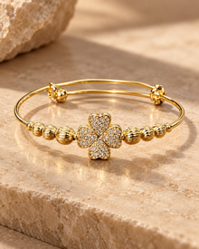 Gold clover bangle bracelet with pavé heart-shaped petals on a warm stone surface