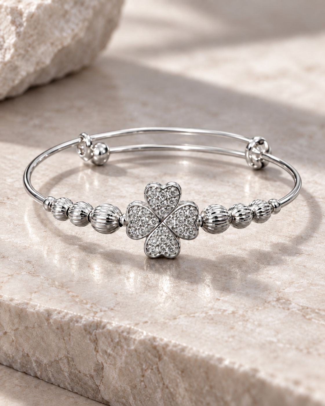 Silver clover bangle bracelet with sparkling heart-shaped petals on a warm stone surface