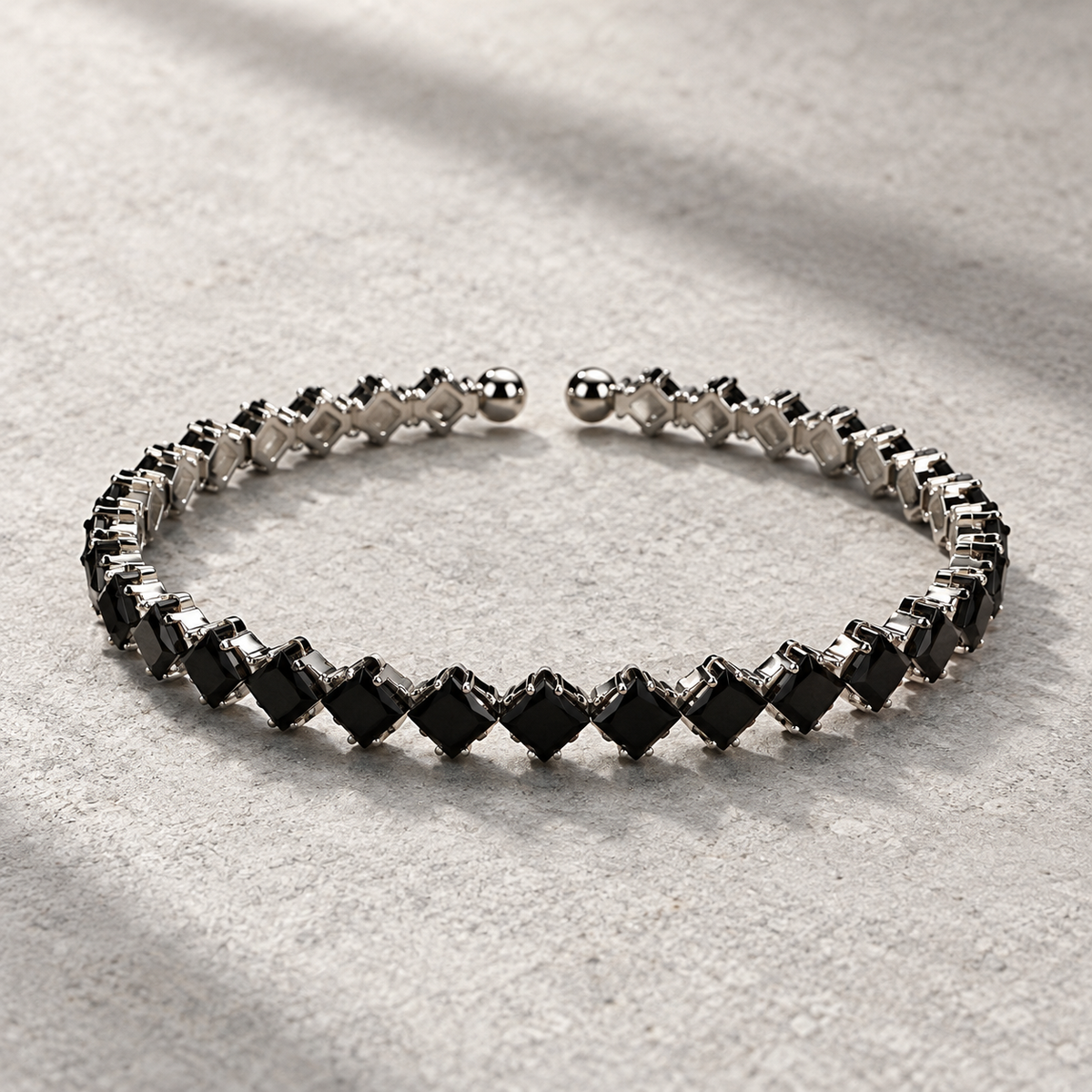 Black Elara Prism Bangle with diagonal square stones, silver-tone settings and rounded open-cuff ends.